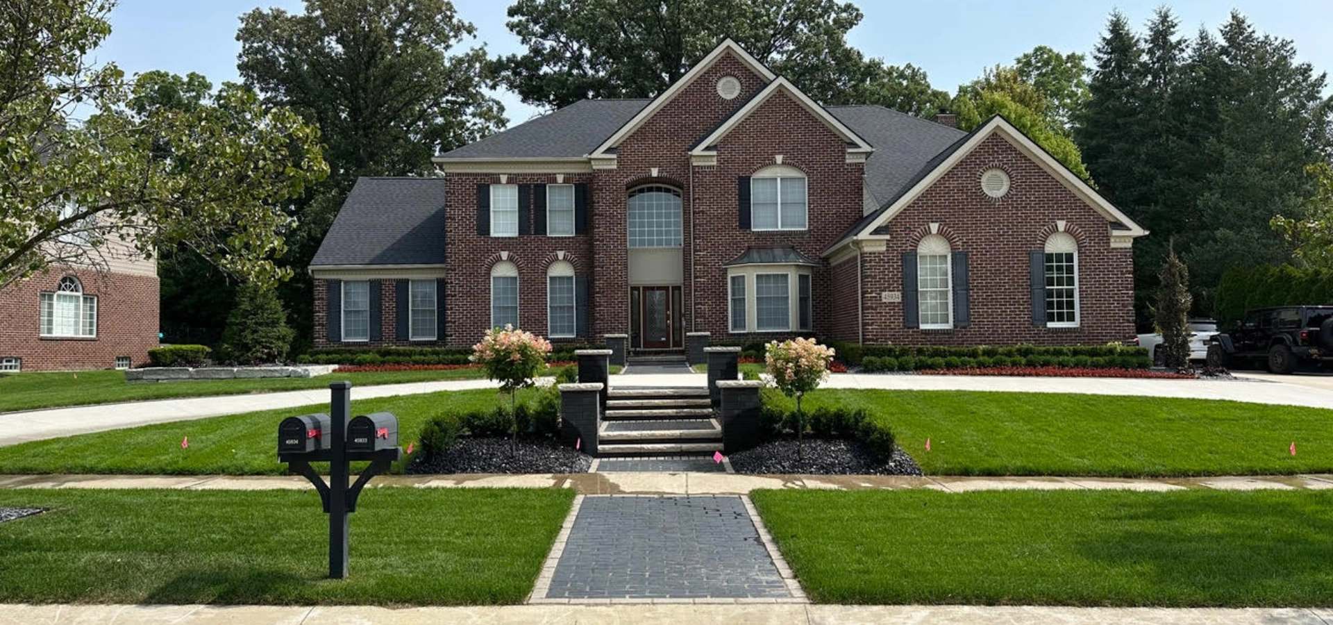front yard landscaping design in northville mi with brick home, walkway, and manicured lawn by blackstone landscaping (248) 939-3600